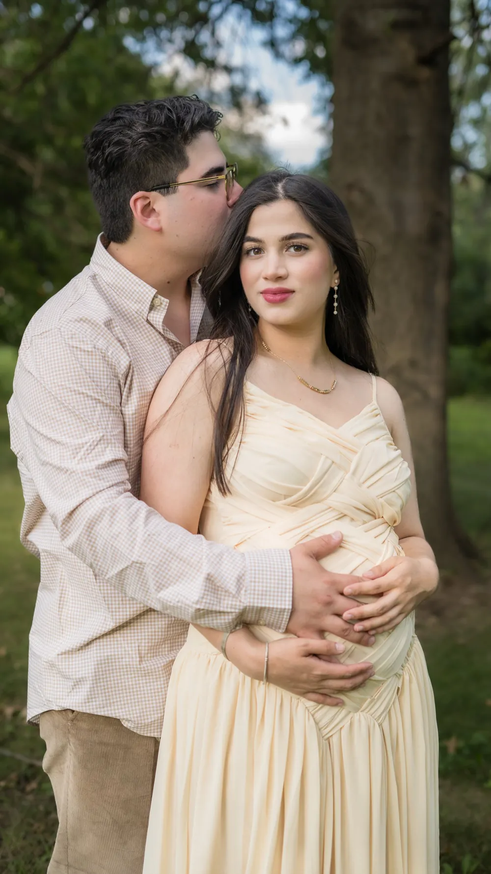 Husband kissing his pregnant wife on the temple as they embrace in a park